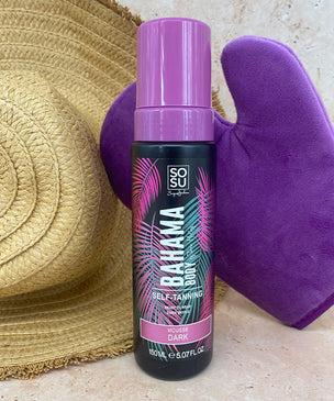 A Bahama Body self-tanning product in a dark shade, alongside a purple tanning mitt and a woven sunhat.