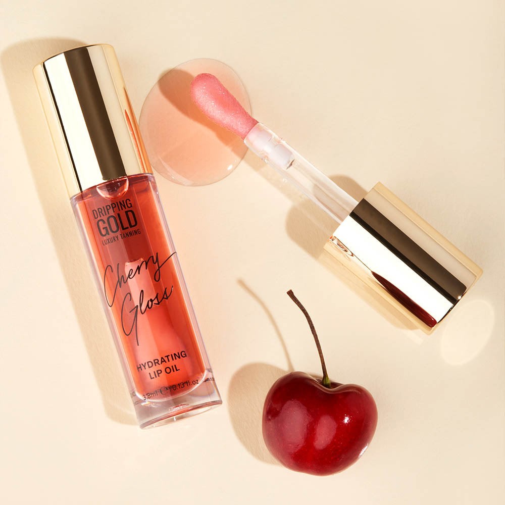 A bottle of Cherry Gloss Hydrating Lip Oil from the Dripping Gold Luxury Tanning collection, designed to provide ultra-soft, glowy lips with its non-sticky, non-greasy texture