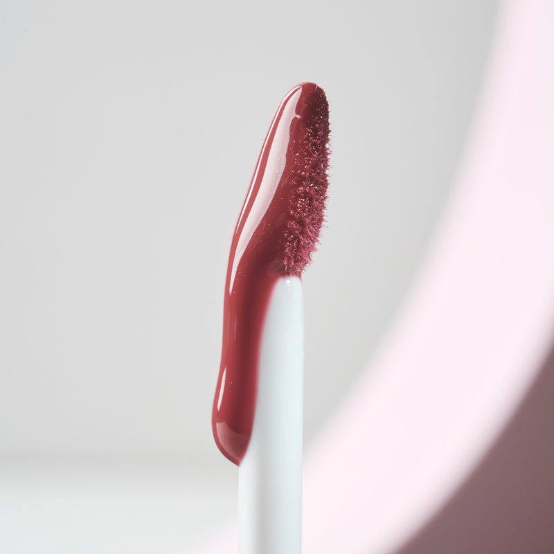 Close-up of the SOSU x Bonnie Ryan lip gloss applicator, displaying the rich rosy pink hue and its velvety texture against a soft pastel background.