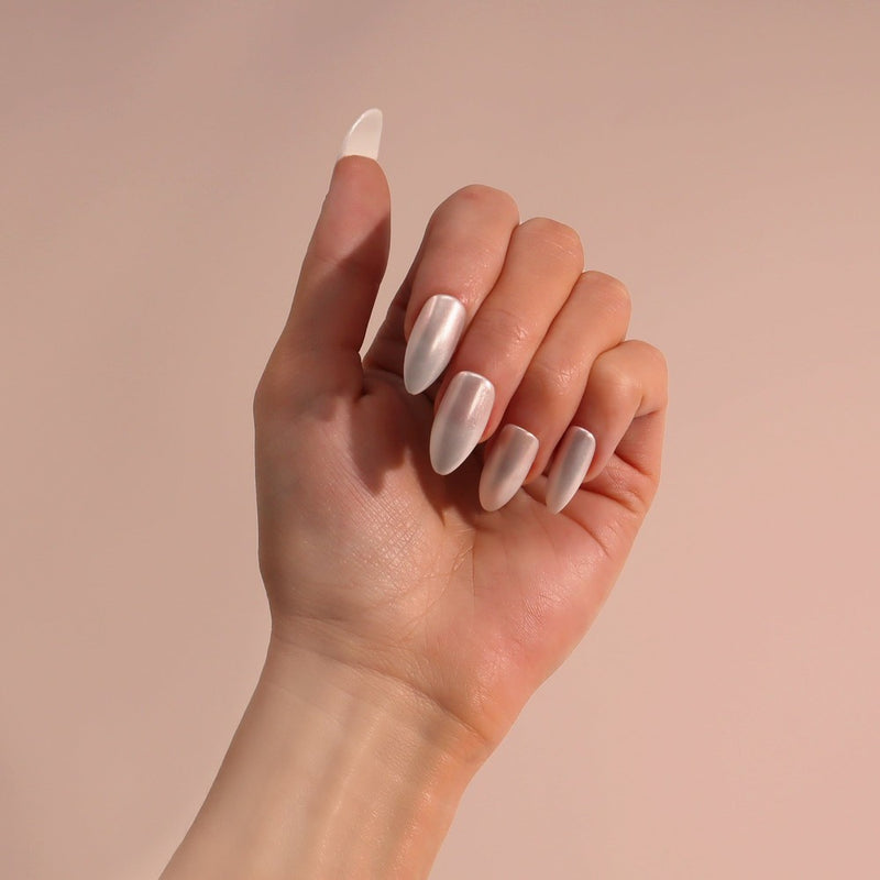 A hand showcasing Milk Glazed Nails, featuring a high gloss, glazed chrome effect in a modern almond stiletto shape. Includes 24 nails in 12 sizes, adhesive, mini nail file, and manicure stick.