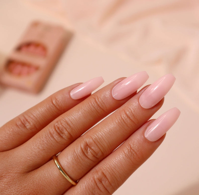 A hand wearing the Nude Desire nail set, a medium-length ballerina shape nail with a rose tint. The set provides a glossy, salon-quality finish and is cruelty-free and vegan friendly.