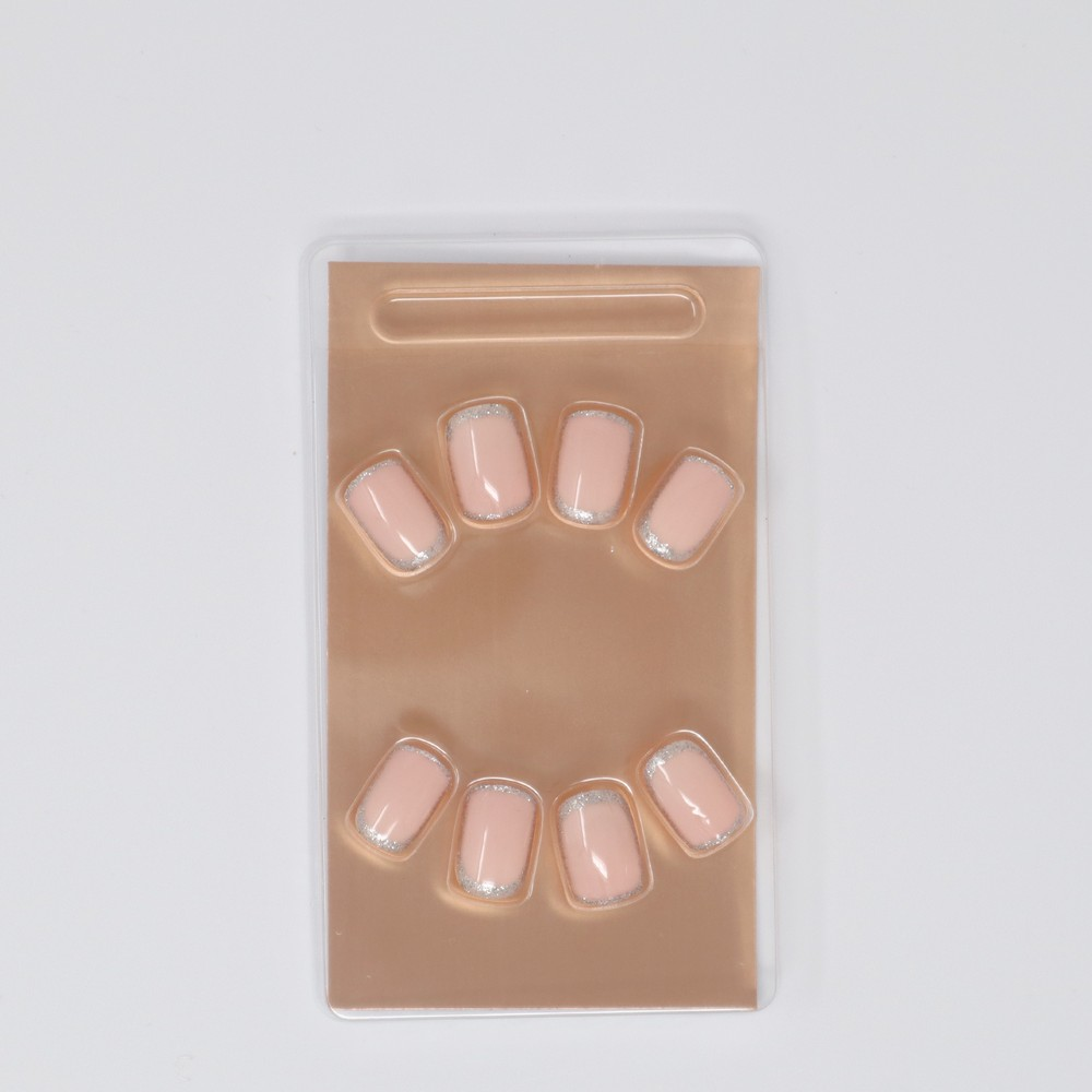 A set of Shy Girl nails with a classic nude color and silver accent, perfect for adding a sparkle to any look. The set includes 24 nails in 12 sizes, adhesive, mini nail file, and a manicure stick. They are cruelty-free and vegan friendly with an extreme gloss finish.