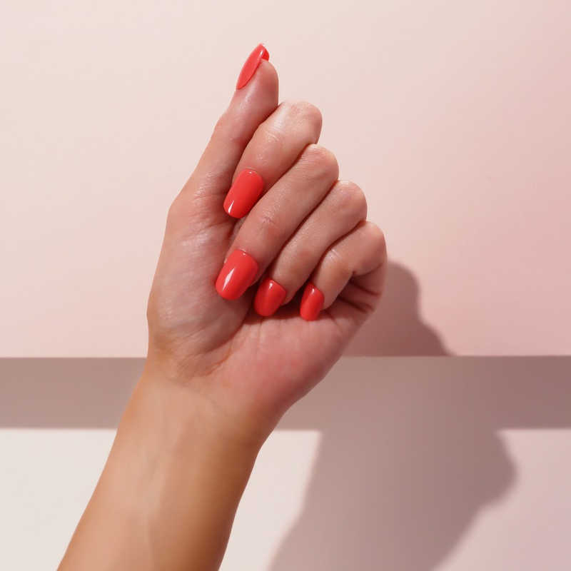 A hand showcasing Coral Kiss Faux Nails by SOSU Cosmetics, featuring square-shaped, short-length nails in a bold and trendy coral color